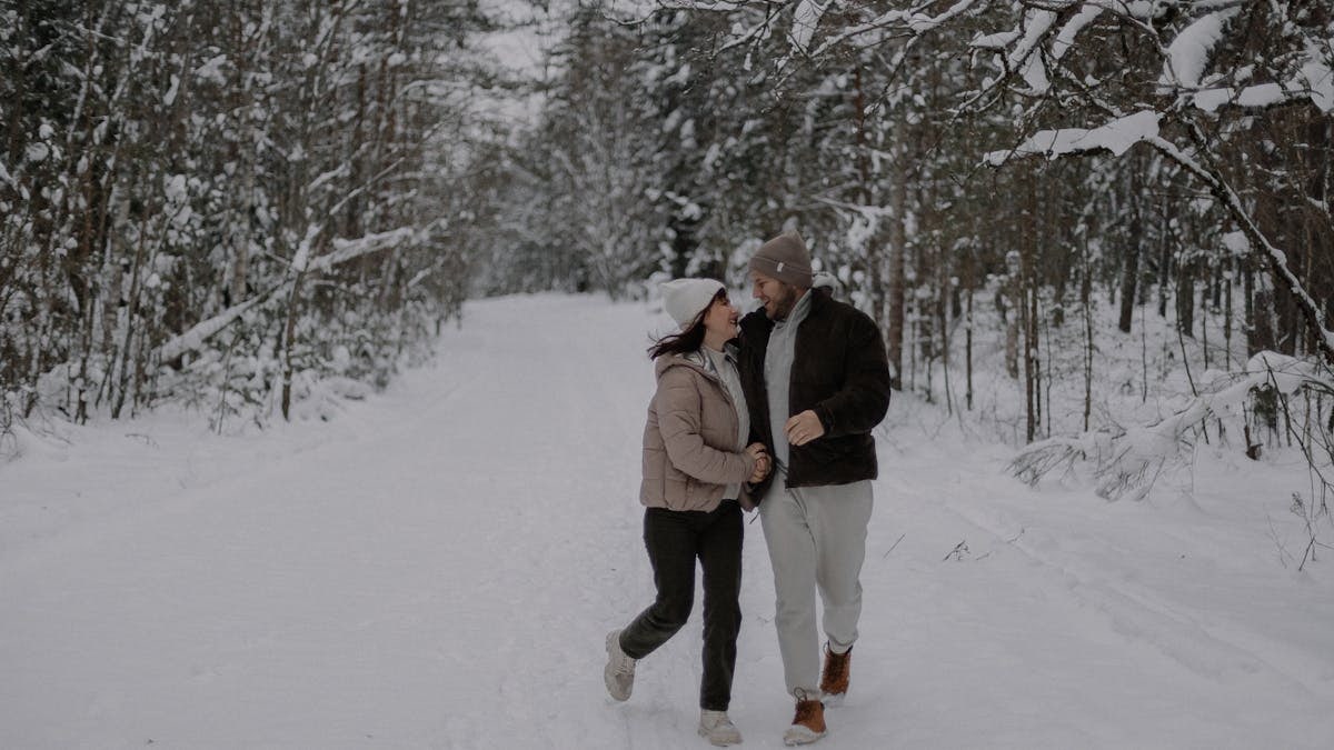 A joyful couple strolls through a snowy forest, embracing winter's beauty and tranquility.