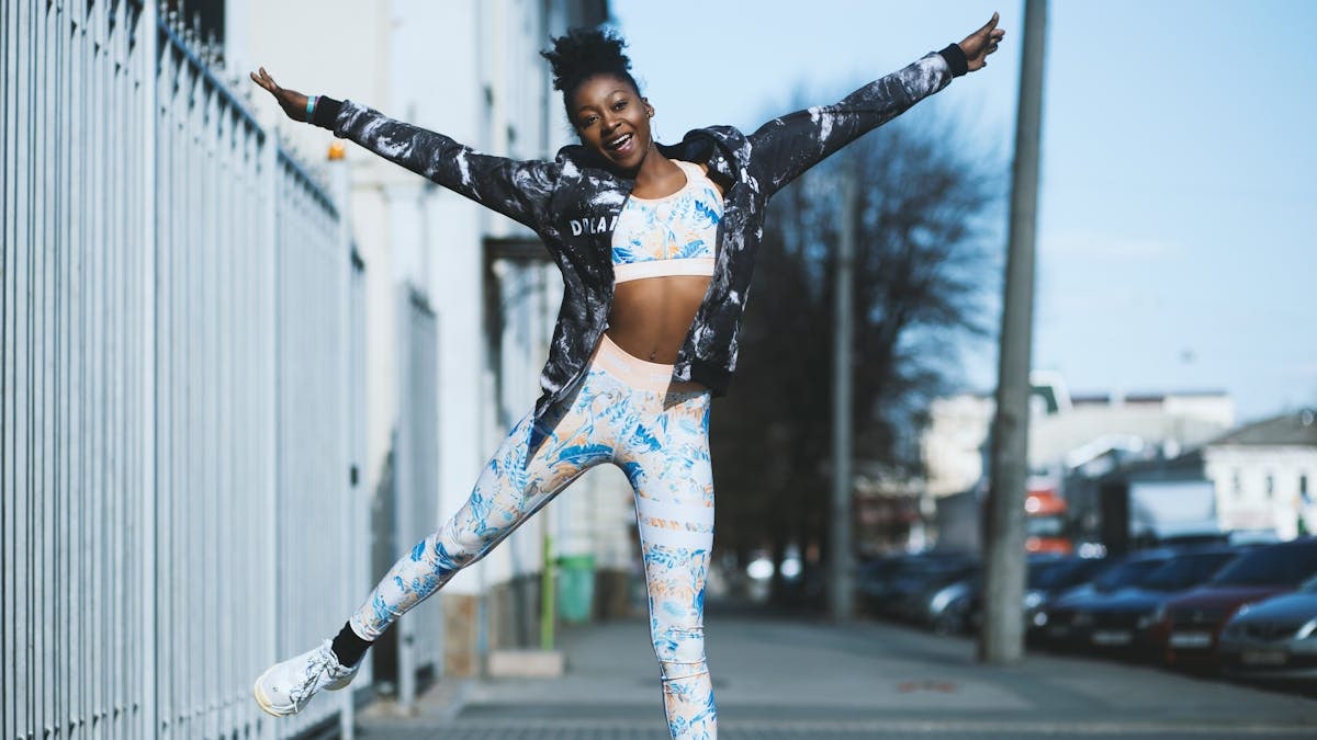Young woman in streetwear joyfully jumping during workout outdoors in city.